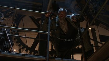 Movie still from “The Hudsucker Proxy” (1994), directed by Ethan Coen – A man in a suit and chains on a metal railing; Wide shot, Low angle