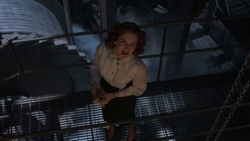 Movie still from “The Hudsucker Proxy” (1994), directed by Ethan Coen – A woman in white shirt and black skirt standing on a metal railing; Medium shot, Overhead angle
