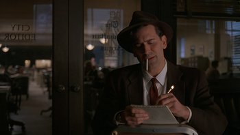 Movie still from “The Hudsucker Proxy” (1994), directed by Ethan Coen – A man in a hat and suit writing in a notebook; Close Up shot, Over the shoulder angle
