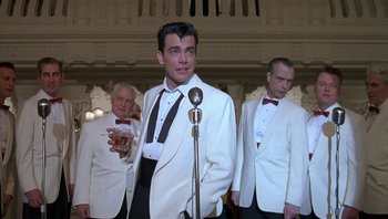 Movie still from “The Hudsucker Proxy” (1994), directed by Ethan Coen – A group of men standing next to each other in tuxedos; Medium shot, Low angle