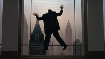 Movie still from “The Hudsucker Proxy” (1994), directed by Ethan Coen – A man standing in front of a large window with his arms outstretched; Wide shot, Low angle