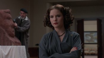 Movie still from “The Hudsucker Proxy” (1994), directed by Ethan Coen – A woman in a gray dress with her arms crossed; Medium shot, Over the shoulder angle