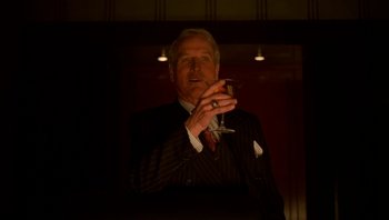 Movie still from “The Hudsucker Proxy” (1994), directed by Ethan Coen – A man in a suit holding a glass of wine; Medium shot, Low angle