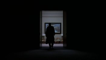 Movie still from “The Hudsucker Proxy” (1994), directed by Ethan Coen – A man standing in front of a painting in a dark room; Extreme Wide shot, Low angle