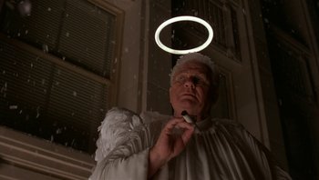 Movie still from “The Hudsucker Proxy” (1994), directed by Ethan Coen – An old man wearing a white angel costume holding an object in the air; Close Up shot, Low angle