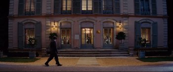 Movie still from “The Hundred-Foot Journey” (2014), directed by Lasse Hallström – A woman walking down the street in front of a building; Extreme Wide shot, Over the shoulder angle
