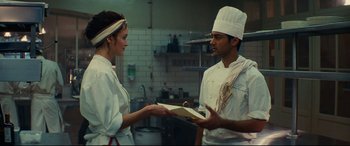 Movie still from “The Hundred-Foot Journey” (2014), directed by Lasse Hallström – A man and a woman in a kitchen holding a book; Medium shot, Over the shoulder angle