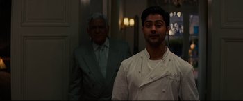 Movie still from “The Hundred-Foot Journey” (2014), directed by Lasse Hallström – A man standing next to another man in a suit; Medium shot, Over the shoulder angle