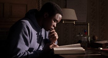 Movie still from “The Hurricane” (1999), directed by Norman Jewison – A man sitting at a table reading a book; Medium shot, Low angle