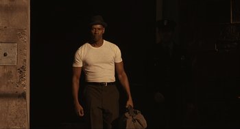 Movie still from “The Hurricane” (1999), directed by Norman Jewison – A man wearing a hat and holding a bag in the dark; Medium shot, Low angle