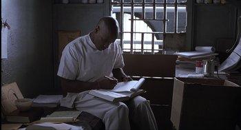 Movie still from “The Hurricane” (1999), directed by Norman Jewison – A man sitting on a chair writing on a book; Medium shot, High angle