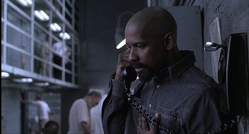 Movie still from “The Hurricane” (1999), directed by Norman Jewison – A man talking on a phone while standing next to a wall; Medium shot, High angle