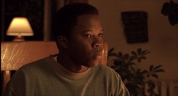 Movie still from “The Hurricane” (1999), directed by Norman Jewison – A man sitting in front of a plant looking at the camera; Close Up shot, Low angle