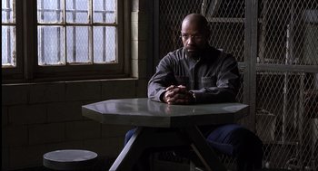 Movie still from “The Hurricane” (1999), directed by Norman Jewison – A man sitting at a table in front of a window; Medium shot, Over the shoulder angle