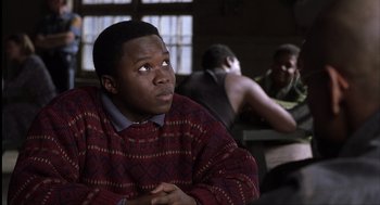 Movie still from “The Hurricane” (1999), directed by Norman Jewison – A man sitting in front of a group of people; Medium shot, Over the shoulder angle