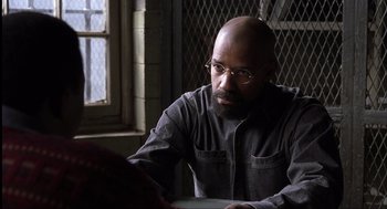 Movie still from “The Hurricane” (1999), directed by Norman Jewison – A man with a beard and glasses sitting in front of a window; Close Up shot, Over the shoulder angle