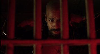 Movie still from “The Hurricane” (1999), directed by Norman Jewison – A bald man with a beard is looking through bars; Close Up shot, High angle