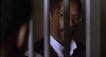 Movie still from “The Hurricane” (1999), directed by Norman Jewison – A person behind bars wearing glasses; Close Up shot, Over the shoulder angle