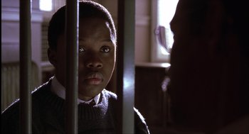 Movie still from “The Hurricane” (1999), directed by Norman Jewison – A young boy is sitting behind bars in a room; Close Up shot, Over the shoulder angle