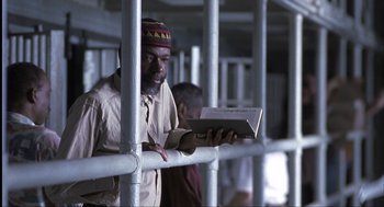Movie still from “The Hurricane” (1999), directed by Norman Jewison – A man reading a book while standing behind bars; Medium shot, Low angle