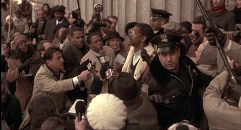 Movie still from “The Hurricane” (1999), directed by Norman Jewison – A group of people gathered in a room with microphones and microphones; Medium shot, Over the shoulder angle