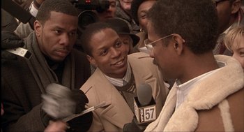 Movie still from “The Hurricane” (1999), directed by Norman Jewison – A group of people gathered around a man with a microphone; Close Up shot, Over the shoulder angle