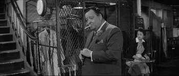 Movie still from “The Hustler” (1961), directed by Robert Rossen – An old photo of a man smoking a cigarette in a suit; Medium shot, Over the shoulder angle