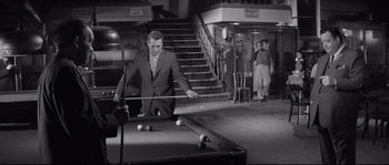 Movie still from “The Hustler” (1961), directed by Robert Rossen – A black and white photo of a man in a suit playing pool; Wide shot, High angle