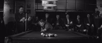 Movie still from “The Hustler” (1961), directed by Robert Rossen – A group of men sitting around a pool table; Wide shot, High angle