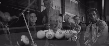 Movie still from “The Hustler” (1961), directed by Robert Rossen – Black and white photograph of a group of men sitting at a pool table; Close Up shot, High angle