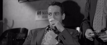 Movie still from “The Hustler” (1961), directed by Robert Rossen – A black and white photo of a man drinking a cup of coffee; Close Up shot, Over the shoulder angle