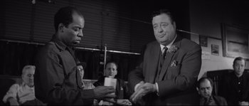 Movie still from “The Hustler” (1961), directed by Robert Rossen – A man in a suit and tie is holding a card; Medium shot, Over the shoulder angle