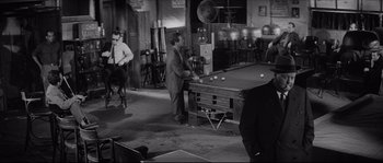Movie still from “The Hustler” (1961), directed by Robert Rossen – Two men playing a game of billiards in an office; Wide shot, Over the shoulder angle
