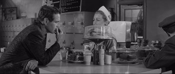 Movie still from “The Hustler” (1961), directed by Robert Rossen – A man and a woman sitting at a table in front of sandwiches; Medium shot, Over the shoulder angle