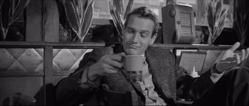 Movie still from “The Hustler” (1961), directed by Robert Rossen – A black and white photo of a man drinking a cup of coffee; Close Up shot, Over the shoulder angle