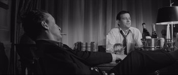 Movie still from “The Hustler” (1961), directed by Robert Rossen – A man smoking a cigarette while sitting next to another man in a suit; Medium shot, Low angle