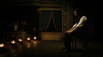 Movie still from “The Illusionist” (2006), directed by Neil Burger – A man sitting on a chair in front of two candles; Wide shot, High angle