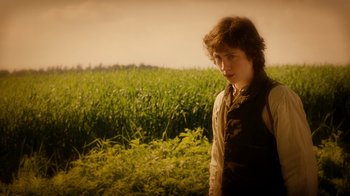 Movie still from “The Illusionist” (2006), directed by Neil Burger – A young man standing in front of a field of green grass; Medium shot, Over the shoulder angle