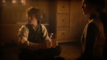 Movie still from “The Illusionist” (2006), directed by Neil Burger – A man sitting on the ground holding a cigarette; Medium shot, High angle