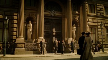 Movie still from “The Illusionist” (2006), directed by Neil Burger – A group of men walking in front of a large building; Extreme Wide shot, Low angle