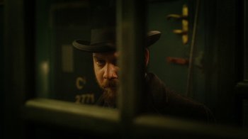 Movie still from “The Illusionist” (2006), directed by Neil Burger – A man with a beard wearing a black hat; Close Up shot, Over the shoulder angle