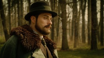 Movie still from “The Illusionist” (2006), directed by Neil Burger – A man with a beard wearing a hat in the woods; Close Up shot, Low angle