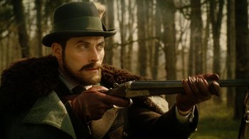 Movie still from “The Illusionist” (2006), directed by Neil Burger – A man with a beard and a hat is holding a gun; Close Up shot, Low angle