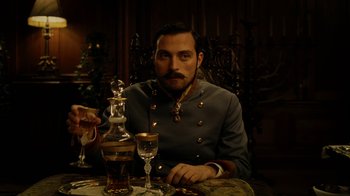 Movie still from “The Illusionist” (2006), directed by Neil Burger – A man sitting at a table with a glass of wine; Medium shot, Low angle