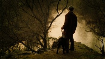 Movie still from “The Illusionist” (2006), directed by Neil Burger – A man and a dog standing next to a body of water; Wide shot, High angle