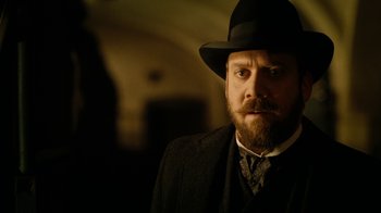 Movie still from “The Illusionist” (2006), directed by Neil Burger – A man with a beard wearing a black hat; Close Up shot, Over the shoulder angle