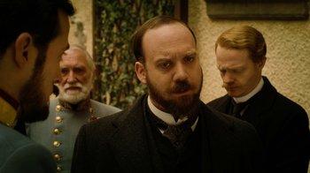 Movie still from “The Illusionist” (2006), directed by Neil Burger – A man with a goatee and a beard standing in front of two other men; Close Up shot, Over the shoulder angle