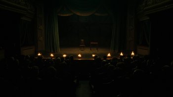 Movie still from “The Illusionist” (2006), directed by Neil Burger – A group of people sitting on a stage in front of a curtain; Extreme Wide shot, High angle