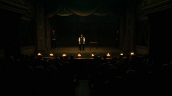 Movie still from “The Illusionist” (2006), directed by Neil Burger – A man sitting on a chair in front of an audience; Extreme Wide shot, High angle