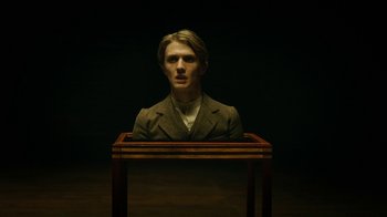 Movie still from “The Illusionist” (2006), directed by Neil Burger – A man in a suit sitting in front of a wooden table; Close Up shot, Low angle